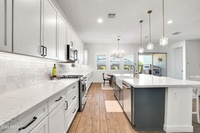 kitchen with pendant lighting, a center island with sink, light hardwood / wood-style flooring, white cabinetry, and appliances with stainless steel finishes