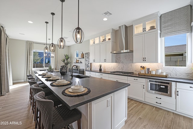 kitchen with white cabinetry, sink, a center island with sink, and wall chimney range hood