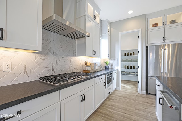 kitchen featuring wall chimney exhaust hood, white cabinetry, tasteful backsplash, light hardwood / wood-style flooring, and appliances with stainless steel finishes