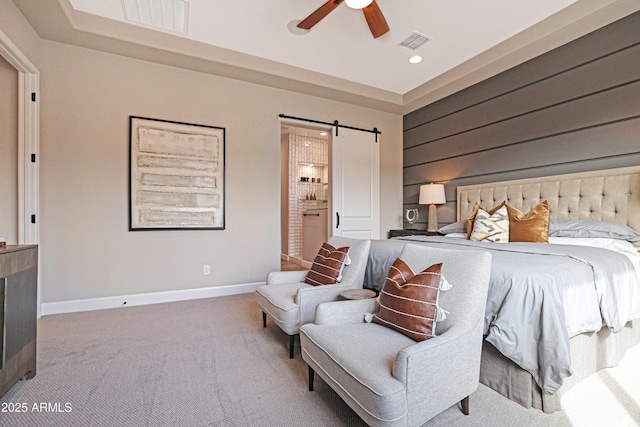 carpeted bedroom with ceiling fan, a barn door, connected bathroom, and wooden walls