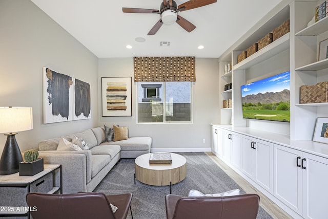 living room featuring built in shelves, ceiling fan, and light wood-type flooring