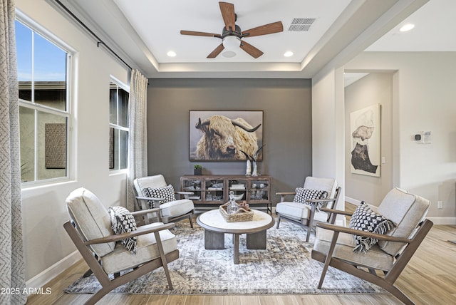 sitting room featuring ceiling fan, wood-type flooring, and a raised ceiling