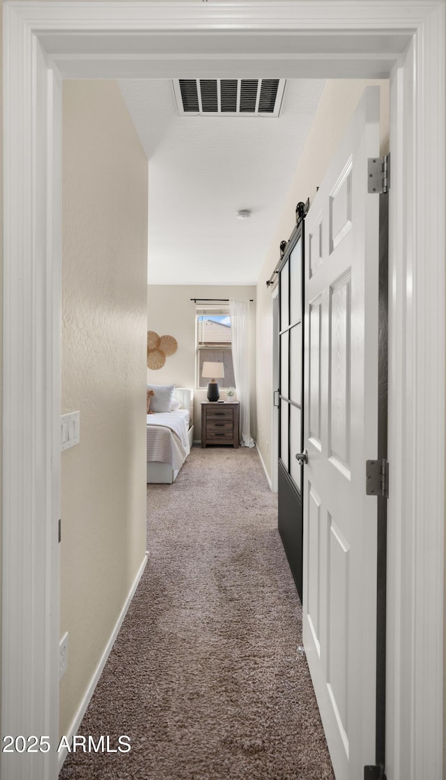 hallway with baseboards, a barn door, visible vents, and carpet flooring