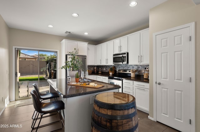 kitchen featuring visible vents, decorative backsplash, appliances with stainless steel finishes, white cabinetry, and a kitchen bar