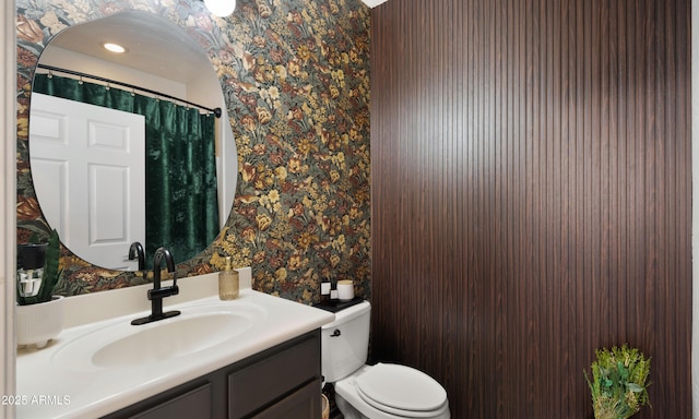 full bathroom featuring toilet, wallpapered walls, and vanity