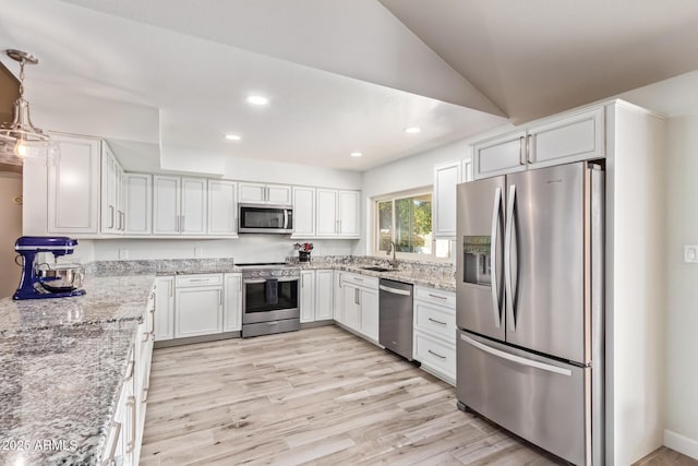 kitchen featuring light wood-style flooring, decorative light fixtures, stainless steel appliances, white cabinetry, and a sink