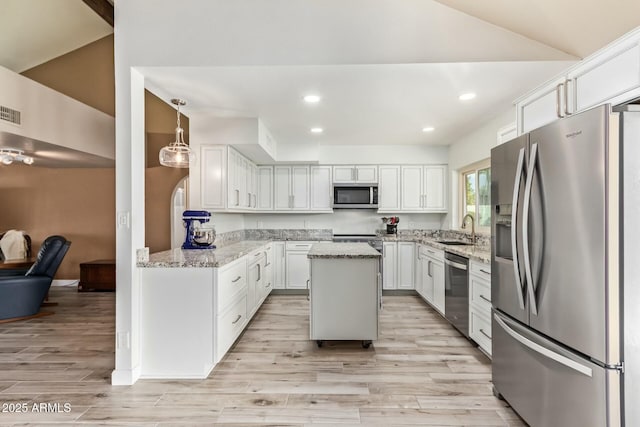 kitchen featuring appliances with stainless steel finishes, light stone counters, a center island, white cabinetry, and a sink