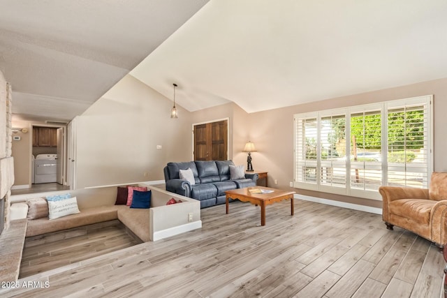 living room featuring vaulted ceiling, light wood-type flooring, washer / dryer, and baseboards