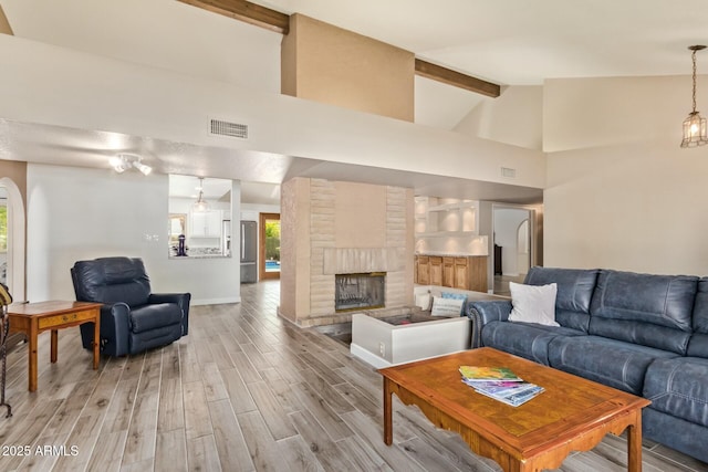 living room with beam ceiling, a fireplace, visible vents, wood finished floors, and high vaulted ceiling