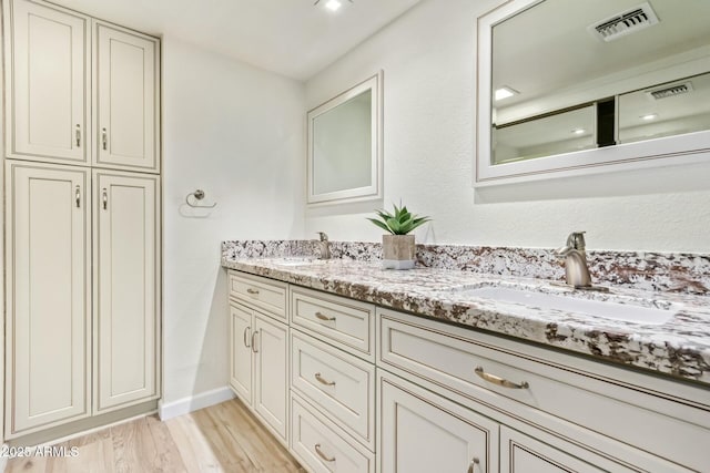 bathroom with wood finished floors, visible vents, a sink, and double vanity