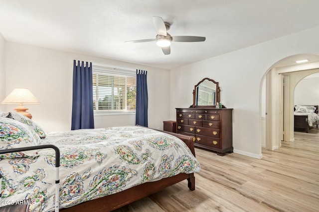 bedroom featuring arched walkways, ceiling fan, light wood-style flooring, and baseboards