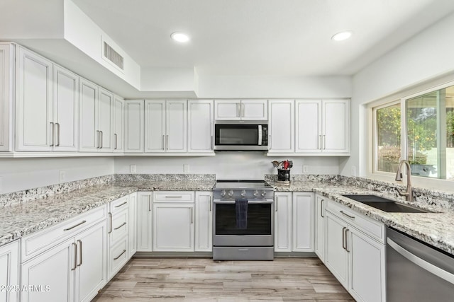 kitchen featuring visible vents, stainless steel appliances, light wood-type flooring, white cabinetry, and a sink