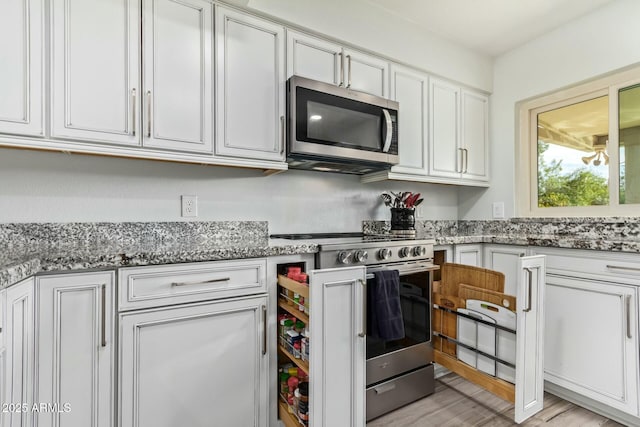 kitchen with appliances with stainless steel finishes, stone countertops, light wood-style flooring, and white cabinets