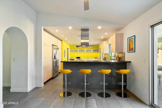 kitchen featuring kitchen peninsula, island exhaust hood, a breakfast bar area, stainless steel refrigerator with ice dispenser, and white cabinets