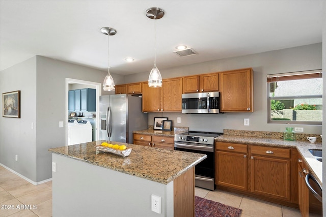 kitchen with light tile patterned floors, appliances with stainless steel finishes, hanging light fixtures, a center island, and light stone countertops