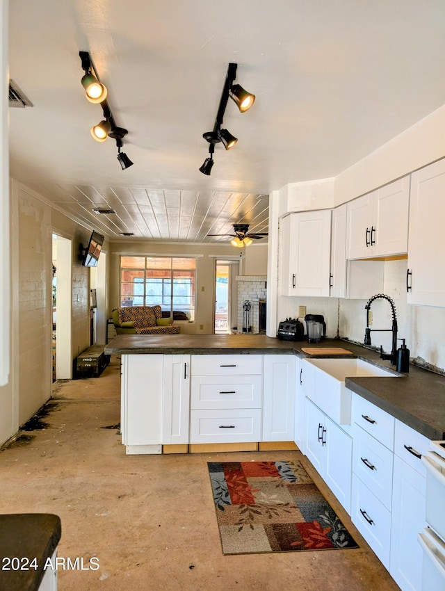 kitchen with a sink, dark countertops, open floor plan, a peninsula, and white cabinets