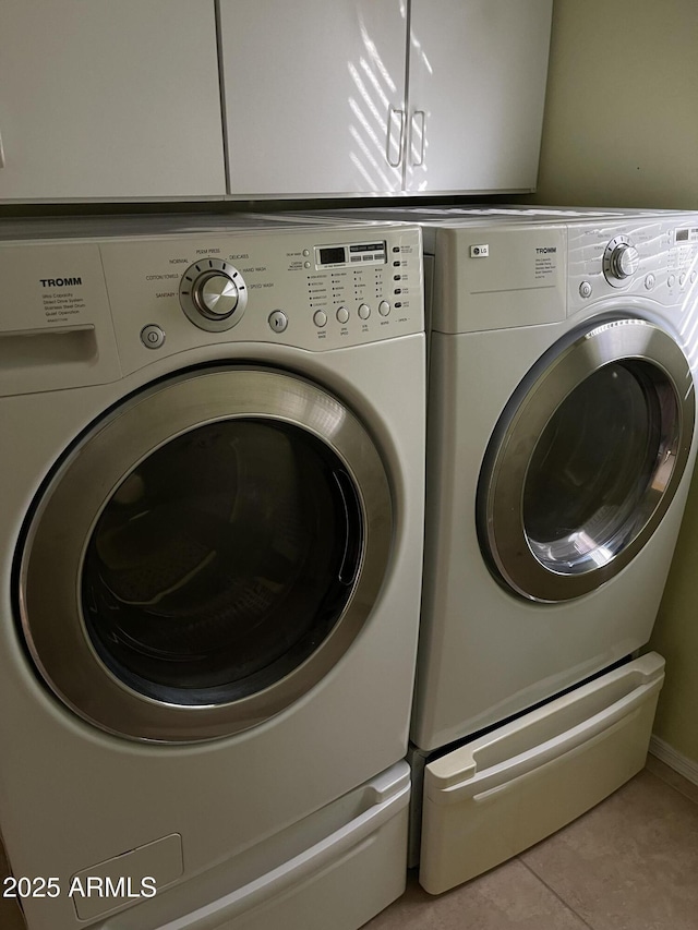 clothes washing area with separate washer and dryer, light tile patterned floors, and cabinets