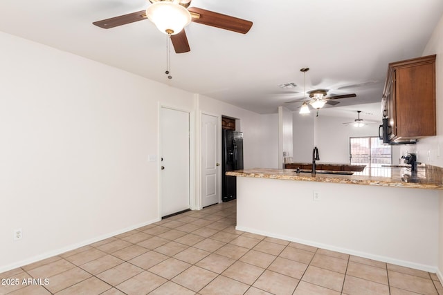 kitchen with kitchen peninsula, sink, light tile patterned floors, black fridge with ice dispenser, and light stone counters