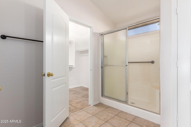 full bath with baseboards, a shower stall, a walk in closet, and tile patterned floors