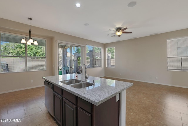 kitchen with light stone countertops, dark brown cabinets, ceiling fan with notable chandelier, sink, and dishwasher