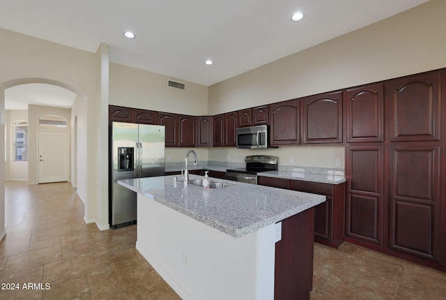 kitchen with light stone countertops, a kitchen island with sink, sink, and stainless steel appliances