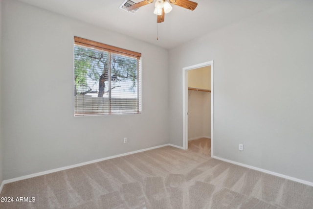 unfurnished bedroom with a spacious closet, a closet, ceiling fan, and light colored carpet