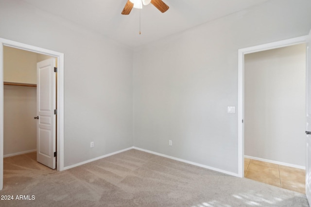 unfurnished bedroom featuring light carpet, a walk in closet, and ceiling fan