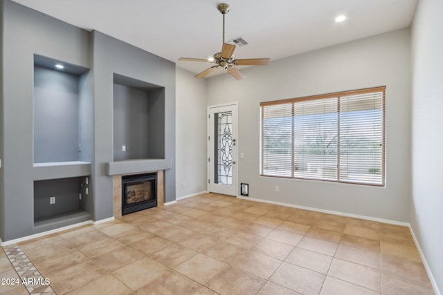 unfurnished living room with ceiling fan, light tile patterned floors, and a tile fireplace