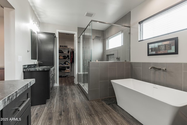 bathroom featuring plus walk in shower, hardwood / wood-style floors, vanity, and tile walls