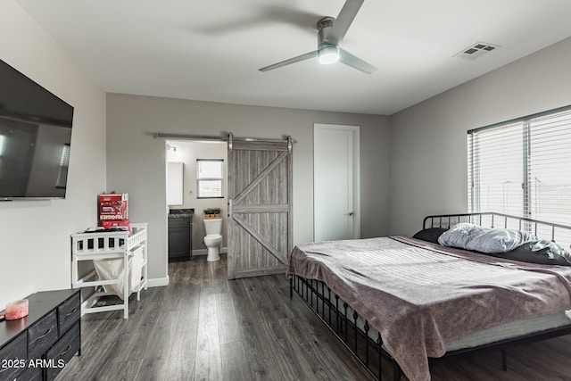 bedroom featuring a barn door, dark hardwood / wood-style floors, ceiling fan, and connected bathroom