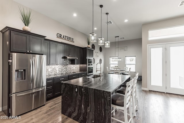 kitchen featuring a breakfast bar, hanging light fixtures, stainless steel fridge, an island with sink, and tasteful backsplash