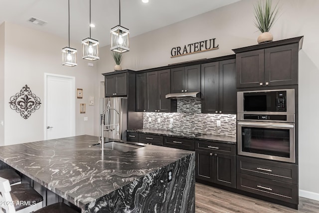 kitchen with pendant lighting, stainless steel appliances, and a center island with sink