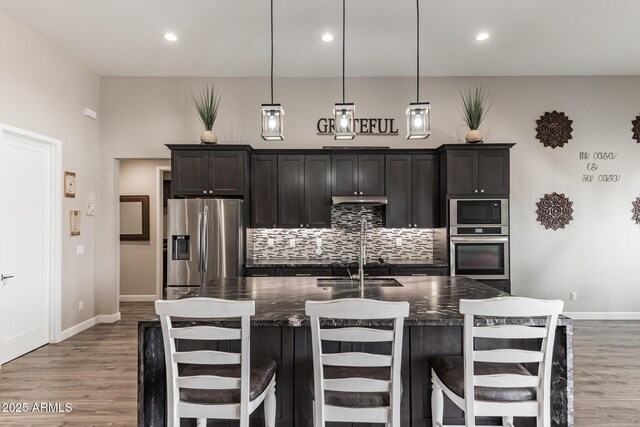 kitchen featuring pendant lighting, a center island with sink, a kitchen breakfast bar, dark stone countertops, and appliances with stainless steel finishes