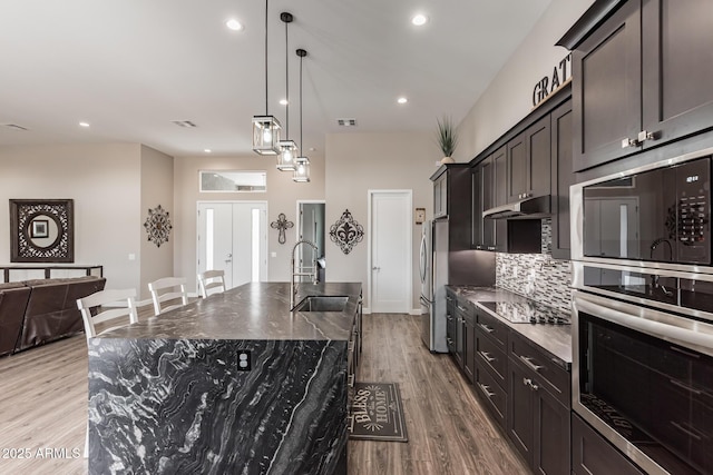 kitchen featuring sink, stainless steel fridge, an island with sink, decorative light fixtures, and light hardwood / wood-style floors