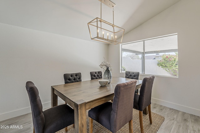 dining area with light wood-type flooring, an inviting chandelier, baseboards, and lofted ceiling