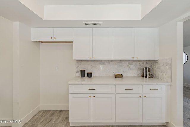 kitchen with tasteful backsplash, visible vents, light wood-style flooring, white cabinetry, and baseboards