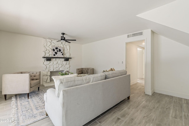 living room featuring baseboards, visible vents, a ceiling fan, light wood-style flooring, and a stone fireplace