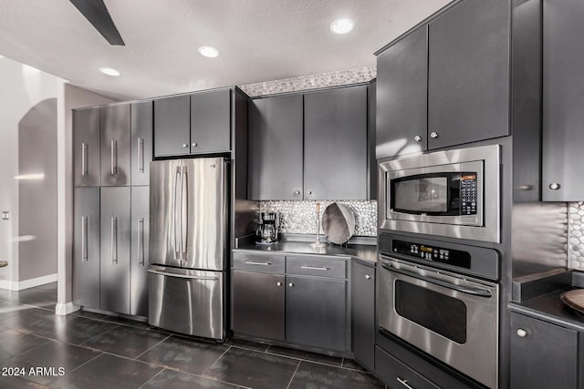 kitchen with a textured ceiling, stainless steel appliances, dark tile patterned flooring, and tasteful backsplash