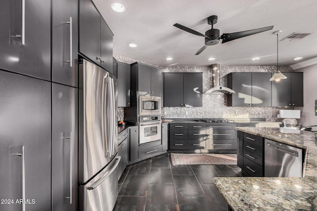 kitchen featuring wall chimney range hood, hanging light fixtures, ceiling fan, tasteful backsplash, and stainless steel appliances