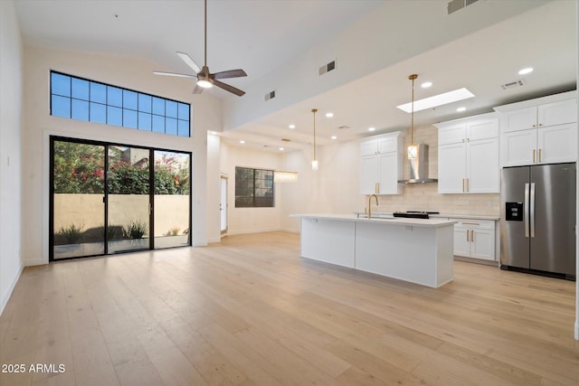 kitchen featuring an island with sink, wall chimney exhaust hood, stainless steel fridge with ice dispenser, and white cabinets