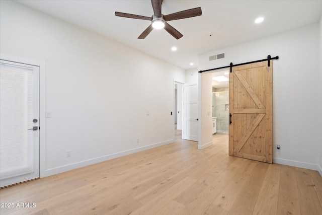 empty room featuring a barn door, ceiling fan, and light wood-type flooring