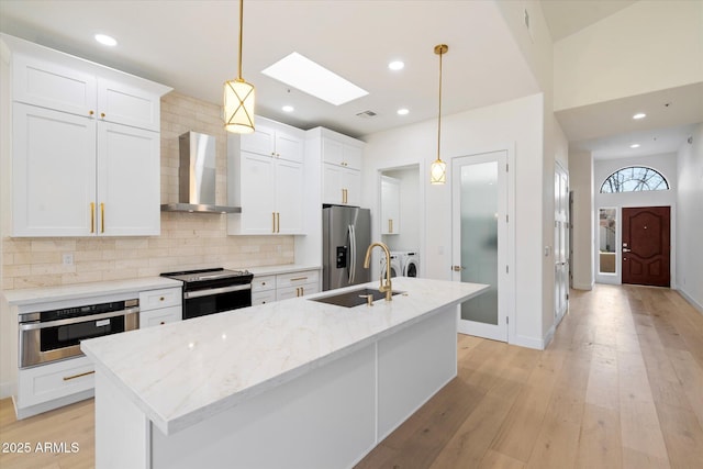 kitchen with wall chimney exhaust hood, white cabinetry, hanging light fixtures, stainless steel appliances, and washing machine and dryer