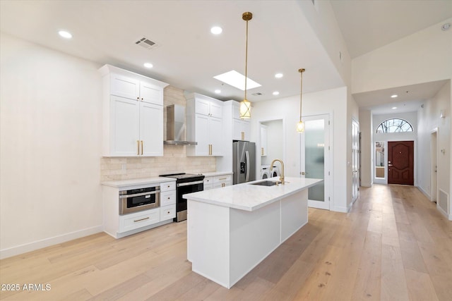 kitchen with appliances with stainless steel finishes, sink, white cabinets, hanging light fixtures, and wall chimney range hood