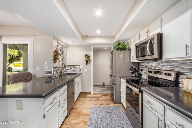 kitchen with sink, appliances with stainless steel finishes, a tray ceiling, white cabinets, and backsplash