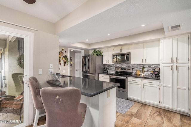 kitchen featuring white cabinetry, stainless steel appliances, a kitchen bar, decorative backsplash, and kitchen peninsula