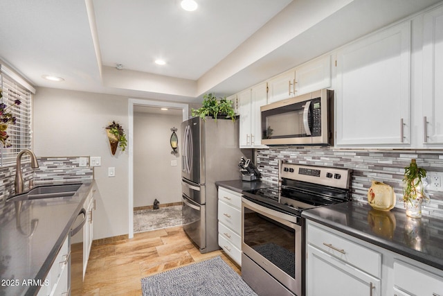 kitchen with a raised ceiling, sink, white cabinets, decorative backsplash, and stainless steel appliances