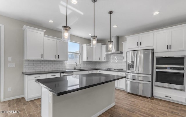 kitchen with appliances with stainless steel finishes, white cabinetry, sink, hanging light fixtures, and wall chimney range hood