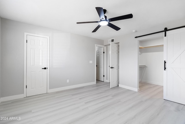 unfurnished bedroom with ceiling fan, a barn door, a walk in closet, and light hardwood / wood-style flooring