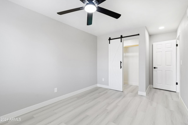 unfurnished bedroom with a barn door, ceiling fan, a closet, and light hardwood / wood-style floors