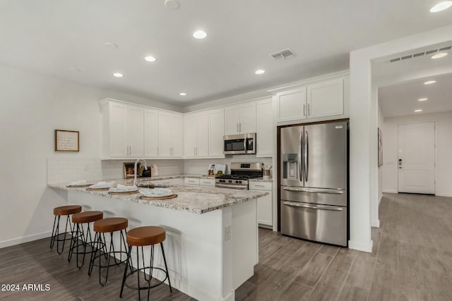 kitchen with white cabinets, stainless steel appliances, kitchen peninsula, and light stone countertops